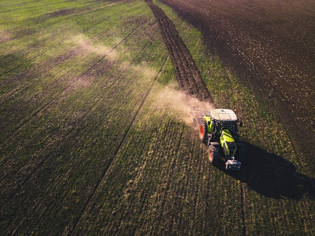 Grön traktor kör över en odlad åker och virvlar upp damm