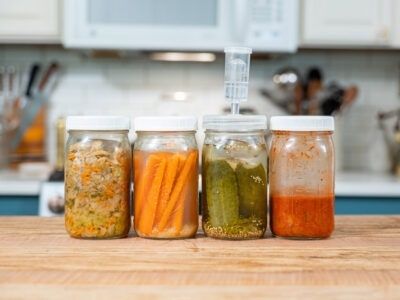 Fyra glasburkar med olika grönsaker och fermenterade blandningar i ett kök