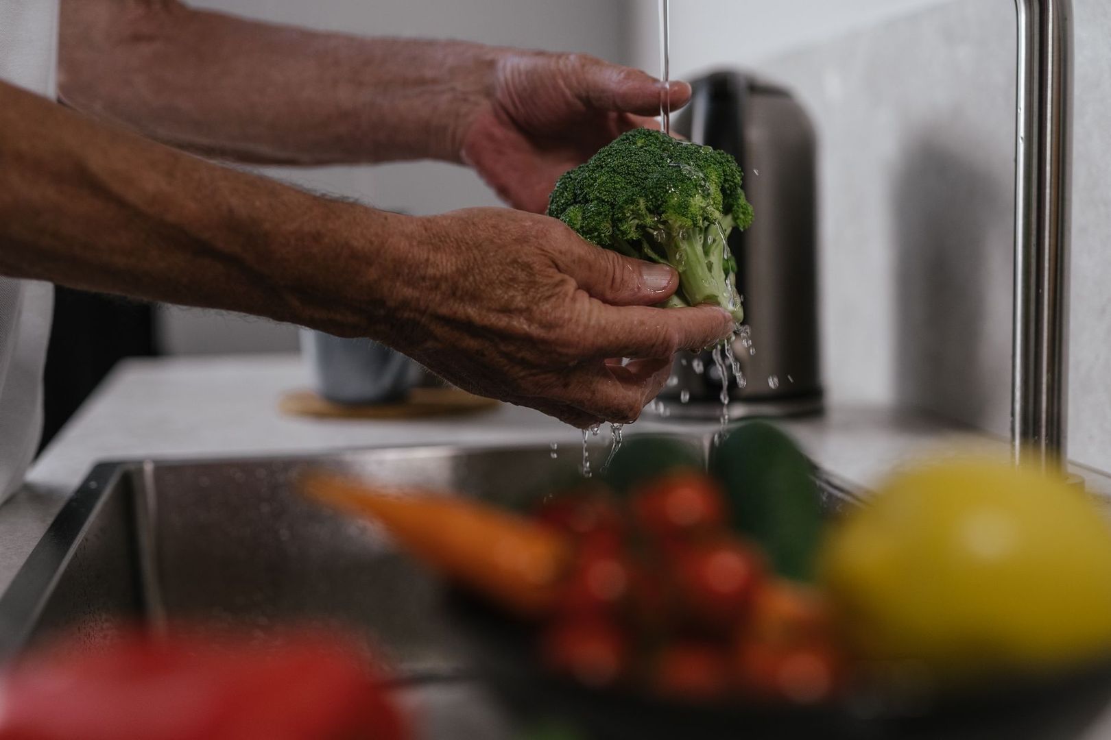 Händer sköljer broccoli under rinnande vatten vid kökskranen